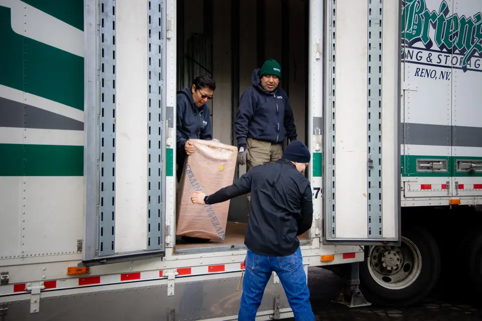 Three O'Brien's movers handing paper-wrapped items out of a moving trailer