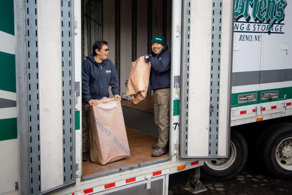 Two O'Brien's movers in a trailer doorway passing a wrapped item