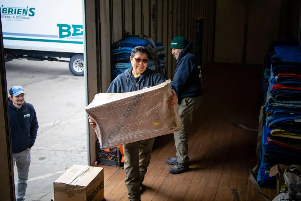 An O'Brien's mover carrying a paper-wrapped item across the warehouse dock