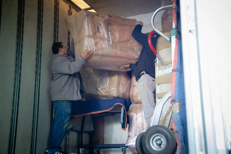 An O'Brien's mover on a ladder stacking paper-wrapped furniture inside a trailer
