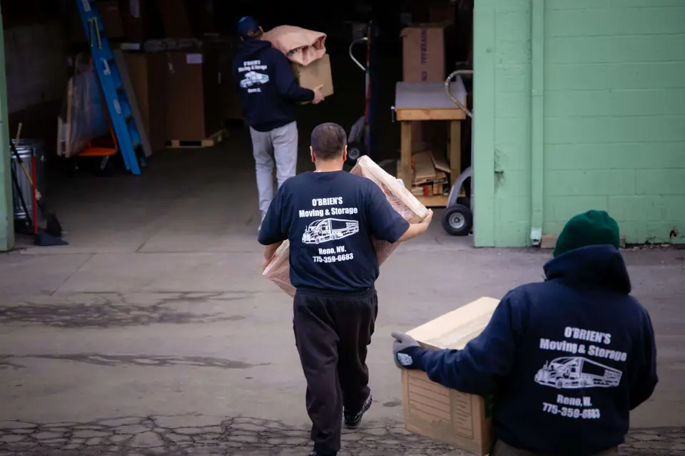 Three O'Brien's movers carrying boxes into the warehouse