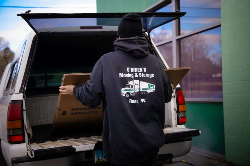 An O'Brien's mover loading flat cartons into a pickup bed