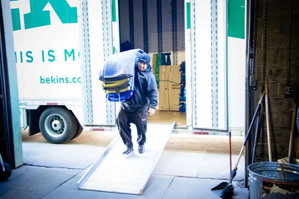 An O'Brien's mover walking down a trailer ramp with furniture pads