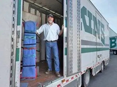An O'Brien's mover standing in the side door of a Bekins trailer stocked with furniture pads