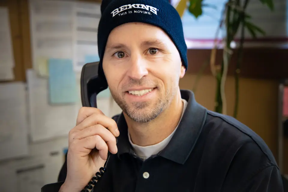 An O'Brien's team member in a Bekins beanie smiling on the phone
