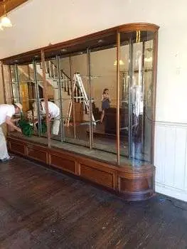 A large antique glass display cabinet being set in place