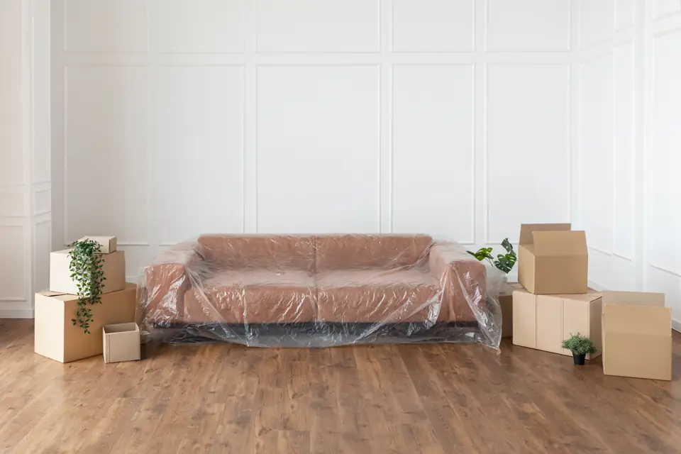 Empty living room with a sofa under protective plastic and stacked moving boxes