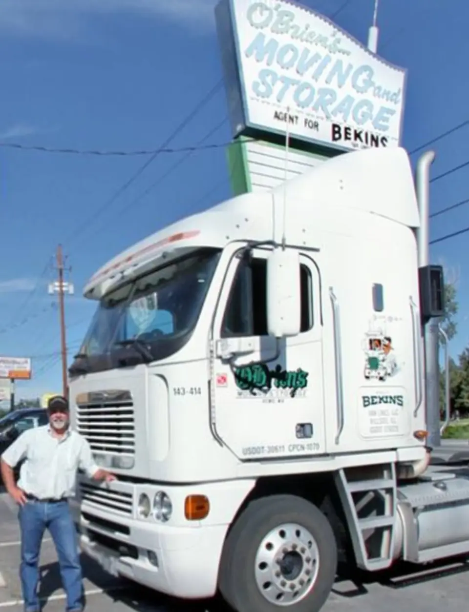 An O'Brien's driver beside a white tractor under the O'Brien's Moving and Storage sign