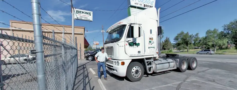 An O'Brien's driver beside a white tractor at the Sparks yard, the O'Brien's sign behind the fence